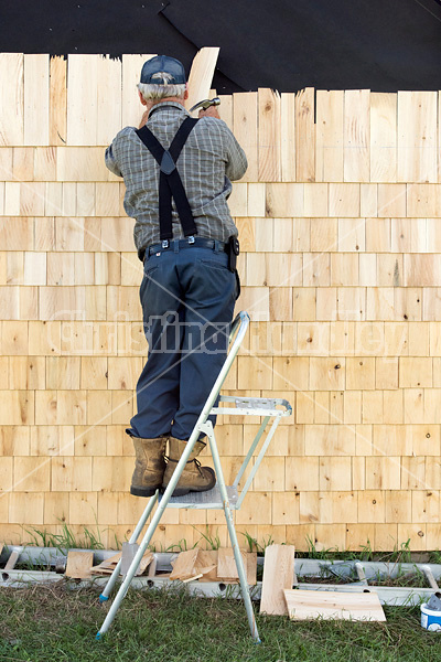 Man putting cedar shingles on the wall of a barn