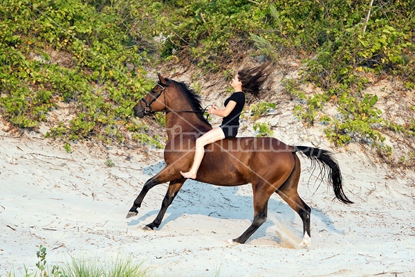 Young woman riding a hrose bareback in the sand