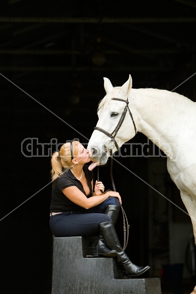 Young woman and white horse posing in barn doorway with black background