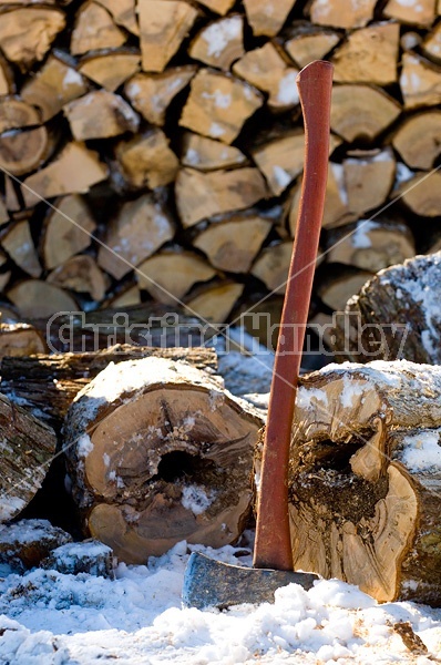Splitting axe leaning against firewood that is cut, split and piled.