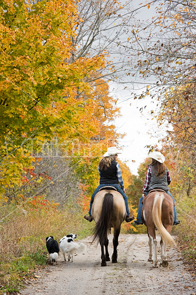 Two young women horseback riding through autumn colored scenery