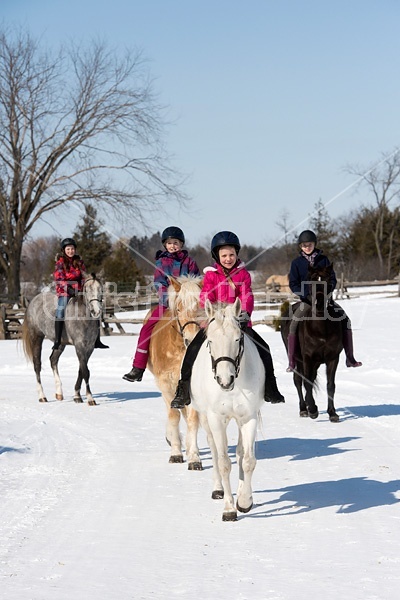 Four young girls riding their ponies bareback in the snow