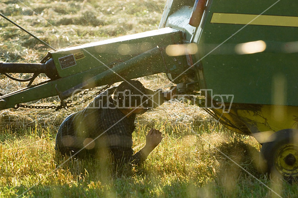 Farmer working underneath round baler to get the twine re-threaded.