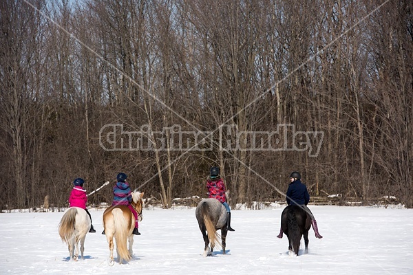 Four young girls riding their ponies bareback in the snow