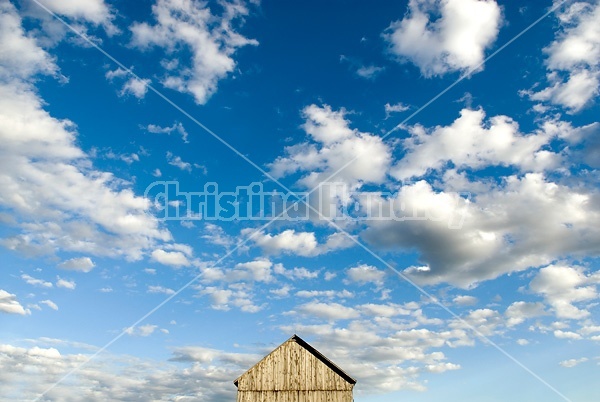 Barn pictured against big blue sky with white puffy clouds