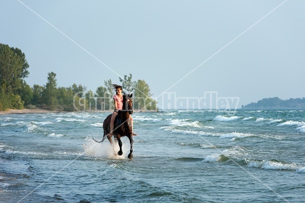 Young woman horseback riding in the surf of Lake Ontario. 