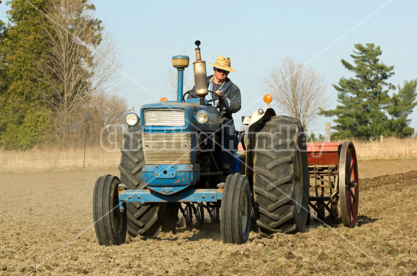 Farmer driving tractor pulling seed drill seeding oats