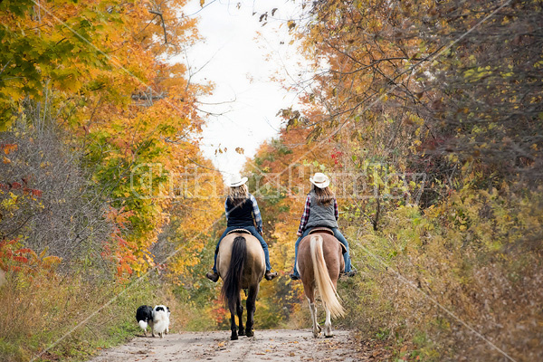 Two young women horseback riding through autumn colored scenery