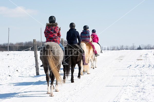 Four young girls riding their ponies bareback in the snow