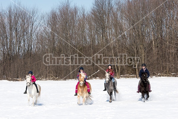 Four young girls riding their ponies bareback in the snow