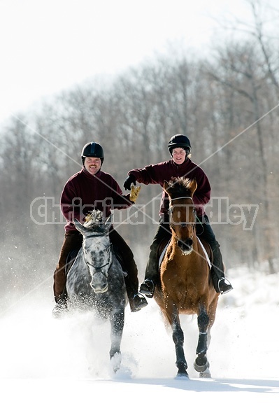 Husband and wife horseback riding through the deep snow holding hands