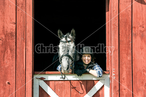 Young woman in barn doorway with horse