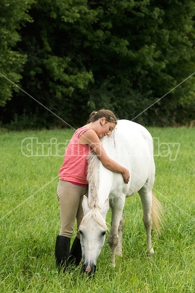 Portrait of a young girl hugging a gray pony in a field