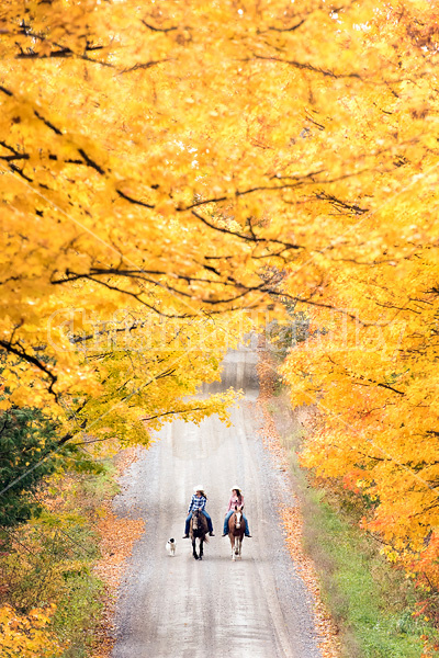 Two young women horseback riding through autumn colored scenery