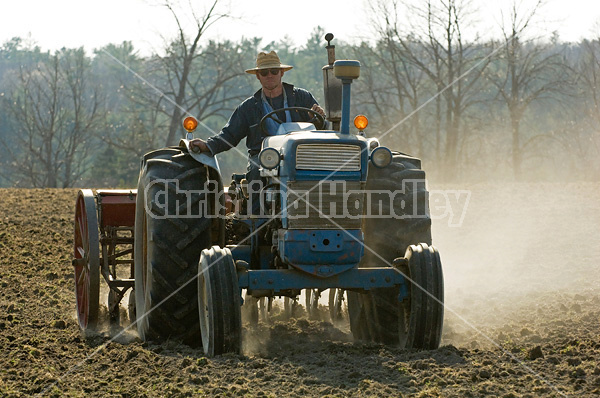 Farmer driving tractor pulling seed drill seeding oats