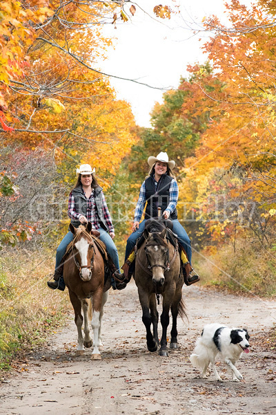 Two young women horseback riding through autumn colored scenery