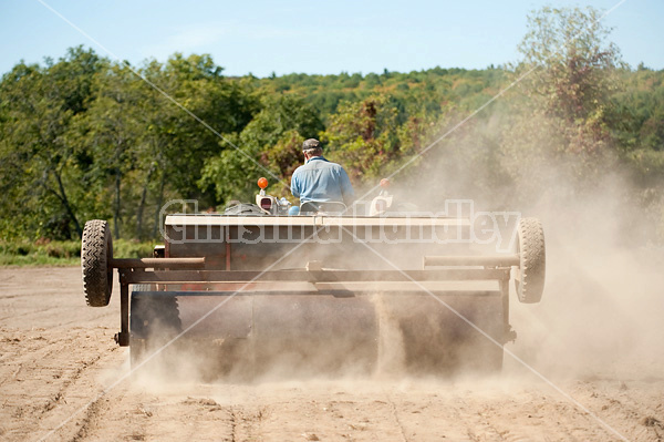 Farmer driving tractor and seed drill seeding oats