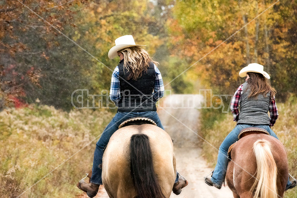 Two young women horseback riding through autumn colored scenery