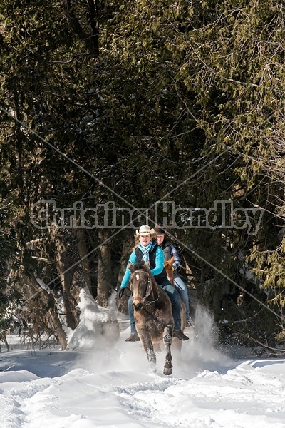 Two young woman riding horses bareback through deep snow