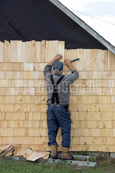 Man putting cedar shingles on the wall of a barn