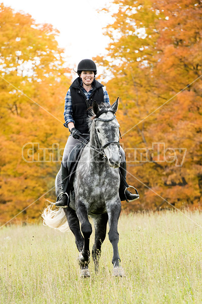 Young woman riding gray horse in the autumn colors