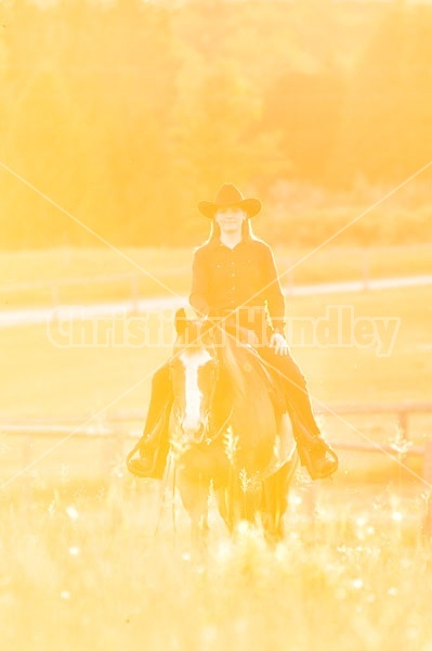 Young woman riding an American Paint Horse mare in the golden glow of the late evening light