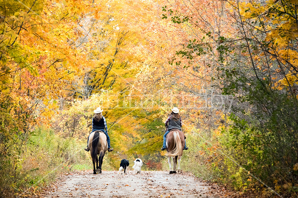 Two young women horseback riding through autumn colored scenery