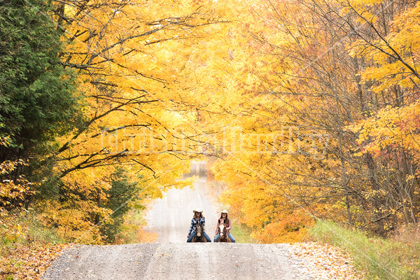 Two young women horseback riding through autumn colored scenery