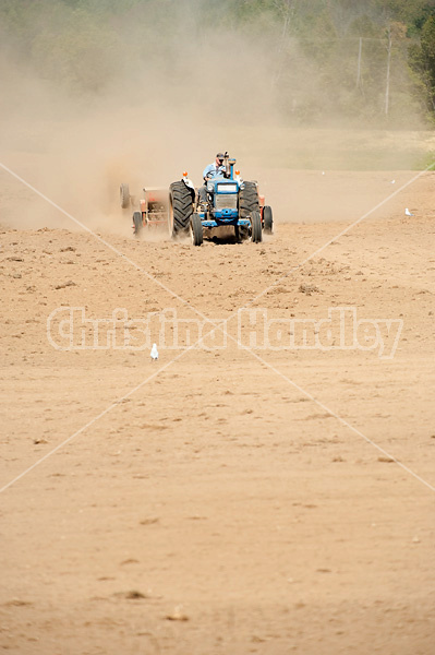 Farmer driving tractor and seed drill seeding oats