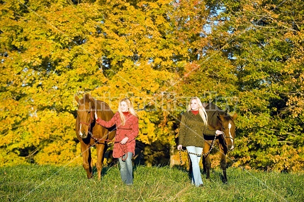 Two women leading horses through field.