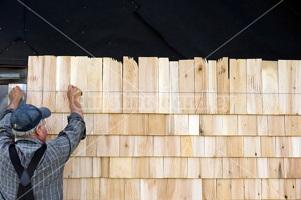 Man putting cedar shingles on the wall of a barn