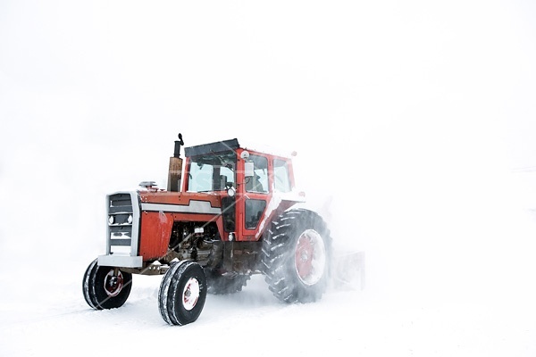 Using tractor and snowblower on a farm to clear snow during a snowstorm.