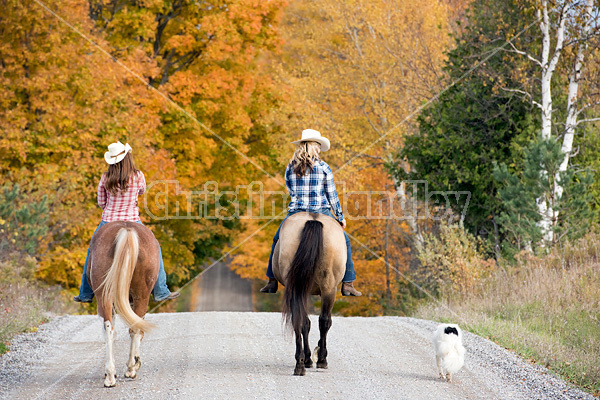 Two young women horseback riding through autumn colored scenery