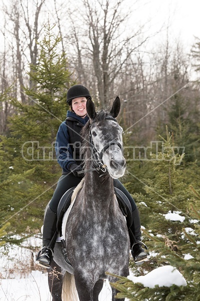 Woman riding Hanoverian mare through forest