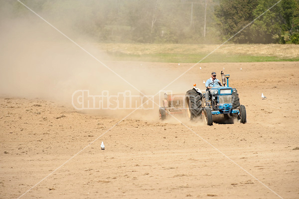 Farmer driving tractor and seed drill seeding oats