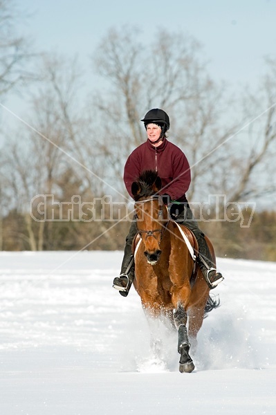 Woman riding bay horse through the deep snow