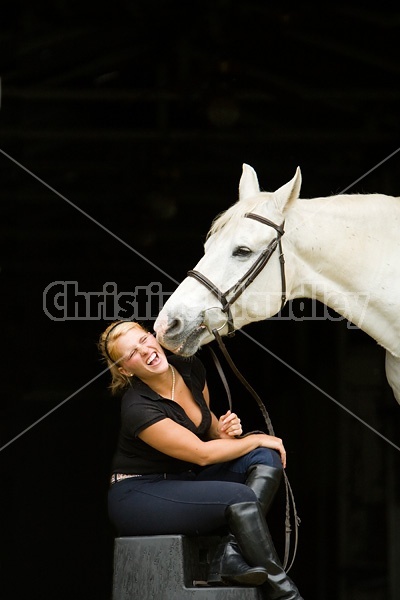 Young woman and white horse posing in barn doorway with black background