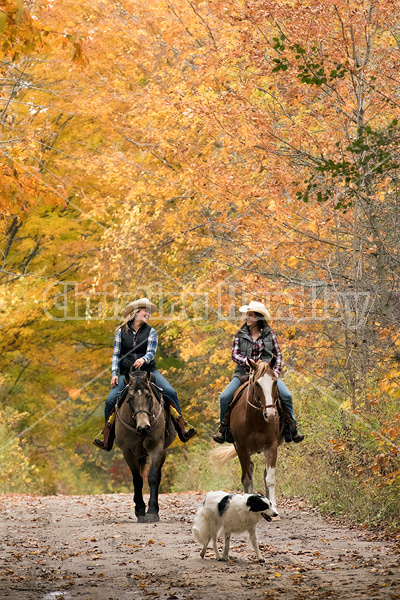 Two young women horseback riding through autumn colored scenery