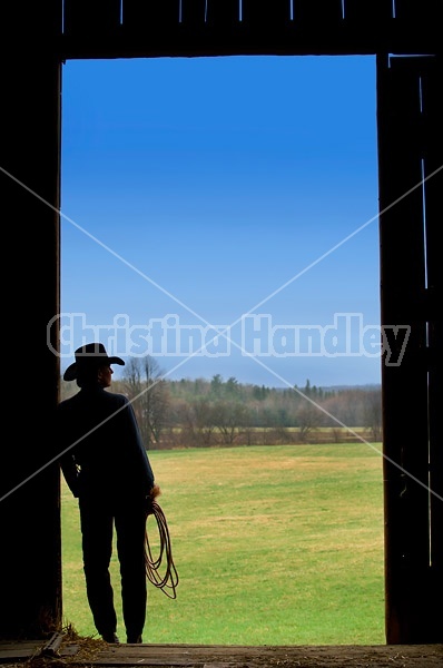 Cowgirl silhouetted in barn doorway