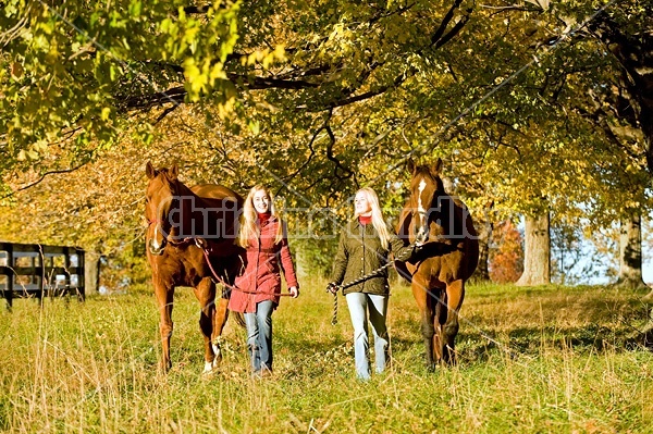 Two women leading horses through field.