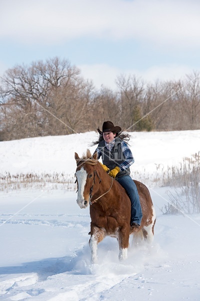 Young woman riding a horse bareback through deep snow