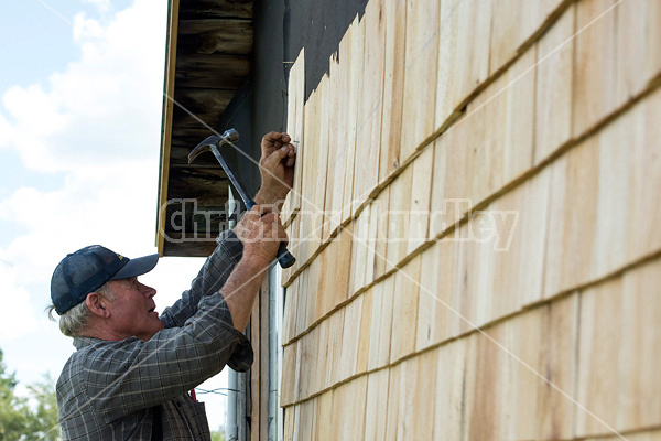 Man putting cedar shingles on the wall of a barn