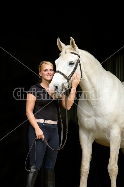 Young woman and white horse posing in barn doorway with black background