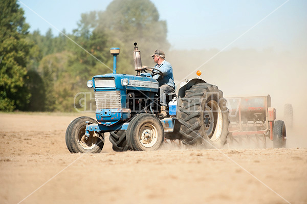 Farmer driving tractor and seed drill seeding oats