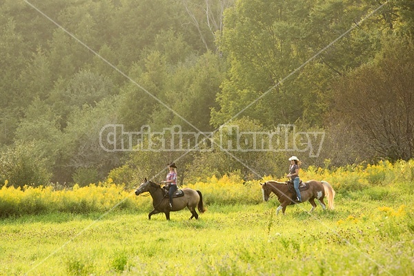 Two young women horseback riding western on a summer evening