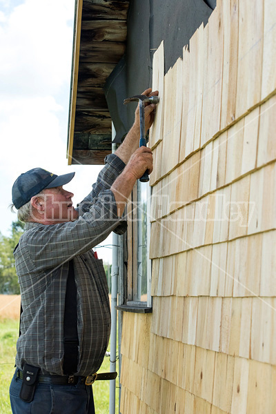 Man putting cedar shingles on the wall of a barn