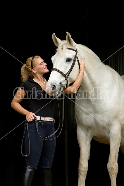 Young woman and white horse posing in barn doorway with black background