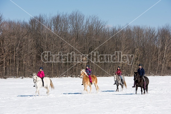 Four young girls riding their ponies bareback in the snow