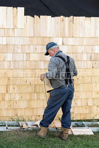 Man putting cedar shingles on the wall of a barn