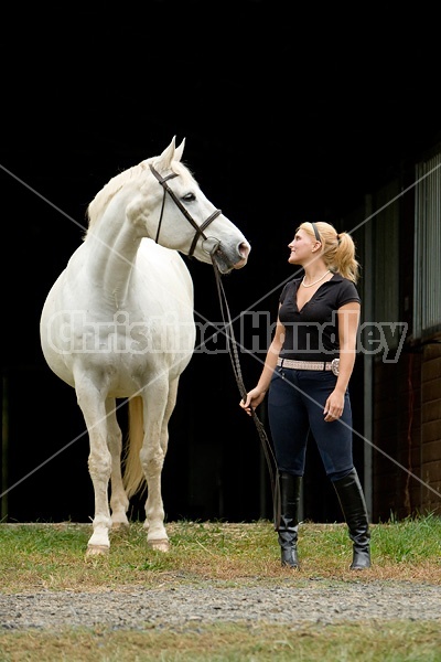 Young woman and white horse posing in barn doorway with black background